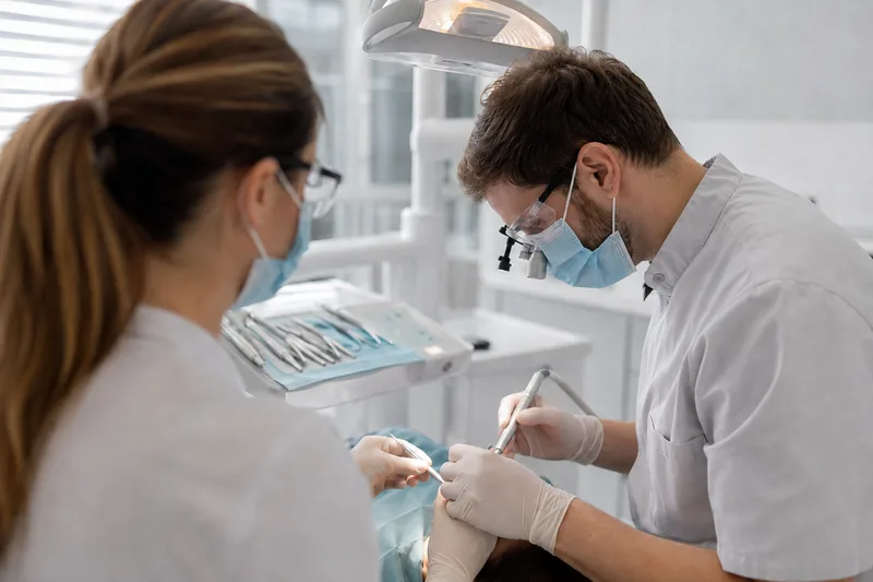 Lekarz dentysta i asystentka w maskach i rękawicach podczas zabiegu
